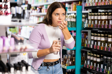 Young girl smelling perfume tester in cosmetics store