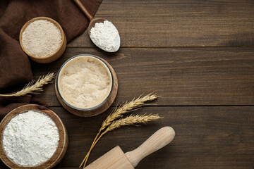 Leaven, flour, rolling pin and ears of wheat on wooden table, flat lay. Space for text