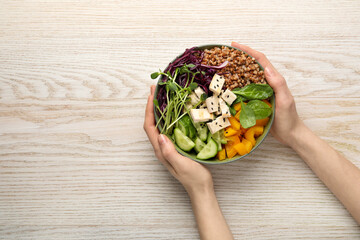 Woman holding delicious vegan bowl with tomatoes, microgreens and buckwheat at white wooden table, top view. Space for text