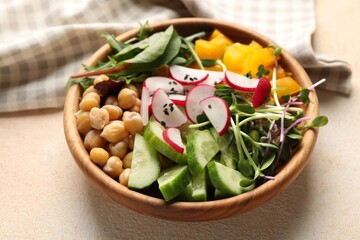 Delicious vegan bowl with cucumbers, chickpeas and radish on beige table, closeup