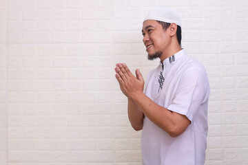 Smiling Asian Muslim man gesturing Eid Mubarak greeting isolated over white background