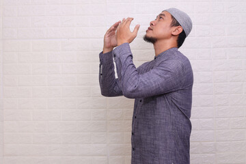 Religious Asian muslim man looking up while praying with opened palms isolated on white background