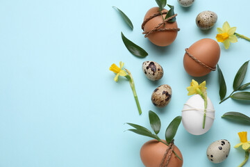 Easter eggs decorated with green leaves and flowers on light blue background, flat lay. Space for text