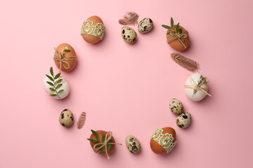 Frame made of festively decorated eggs and natural decor on pink background, top view with space for text. Happy Easter