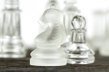 Glass chess pieces on a wooden table with space for a copy. A chess horse made of matte plastic next to a transparent pawn, a board game, a concept.