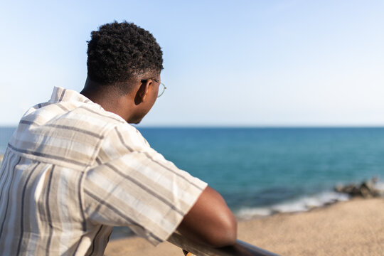 Rear view of pensive african american man relaxing looking at the ocean. Copy space.