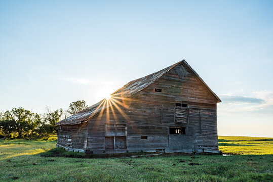 Sunburst over an old, abandoned barn in a prairie pasture at sunset in Saskatchewan, Canada