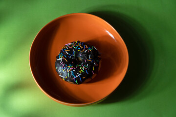 Colourful donuts in orange plate on green background. Top view