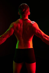 Fashion portrait of an athletic trim attractive man. Manly naked torso in his underpants. Colored flash of studio neon light.