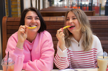 Two women friends eating, smiling and talking in cafe