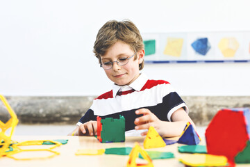 Happy kid boy with glasses having fun with building and creating geometric figures, learning mathematics and geometry