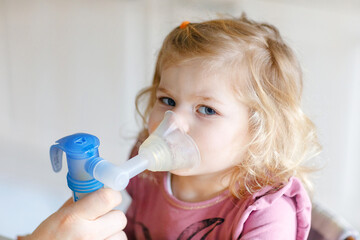 Little toddler girl making inhalation with nebulizer at home. Father or mother helping and holding...