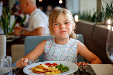 Adorable little girl having breakfast at resort restaurant. Happy preschool child eating healthy food, vegetables and eggs in the morning.