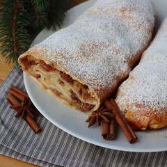 Traditional Apple strudel with cinnamon and powdered sugar on a white plate on wooden table