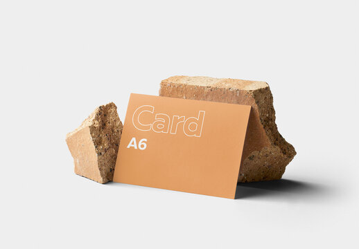 Mockup of customizable horizontal color A6 card resting against rocks available against customizable color background
