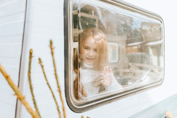 little red haired cute girl looks out the window having fun in cosy bed in trailer mobile home or...