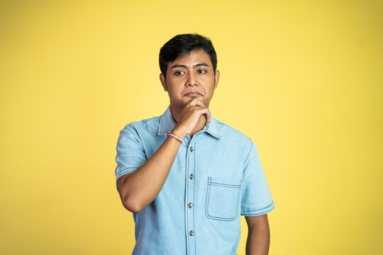 young asian man stand with sardonic expression as hand on chin in isolated background