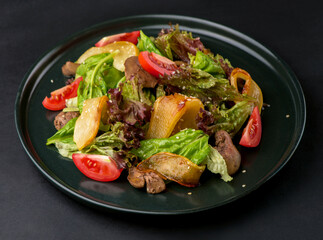 lettuce salad with liver, caramelized pears and tomatoes on a dark background