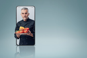 Confident cook holding fresh tasty vegetables and smiling in a smartphone videocall and smiling,...