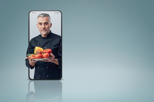 Confident cook holding fresh tasty vegetables and smiling in a smartphone videocall and smiling, online  service concept