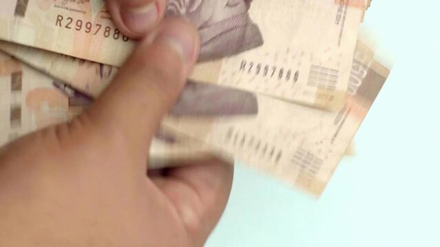 Close-up of fingers counting Mexican 500 Peso bills, blue background