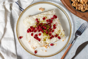 Gullac dessert. Ramadan dessert. Gullac garnished with pomegranate and pistachio in glass plate on gray background. Symbolic food.