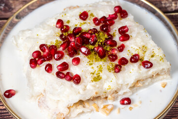 Gullac dessert. Ramadan dessert. Gullac garnished with pomegranate and pistachio in glass plate on wood background. Symbolic food.