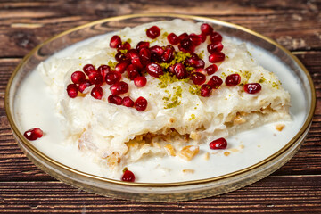 Gullac dessert. Ramadan dessert. Gullac garnished with pomegranate and pistachio in glass plate on wood background. Symbolic food.