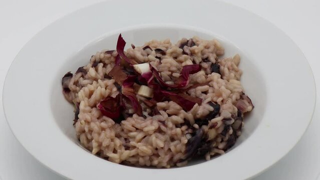 Italian Risotto al radicchio rosso (Risotto with red radicchio) in a white dish, rotating.