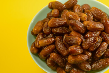 Dates. Dried date palm fruits. Healthy sweet snack food bowl. Pile of tasty dry dattes in plate. Date harvest symbolizing Ramadan. Blue plate on yellow background