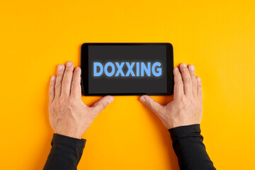 Male hand holds a tablet pc with the word doxxing or doxing on the screen.