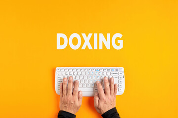Male hands typing the word doxing with a computer keyboard. Doxing or doxxing
