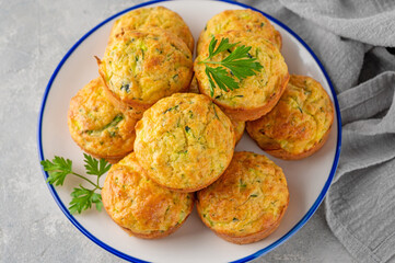 Homemade zucchini muffins with cheese, garlic and herbs on a plate on a gray concrete background. Vegetarian dish. Copy space.