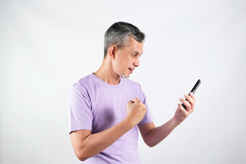 Portrait of a satisfied Asian man with casual purple tshirt celebrating success isolated over white...