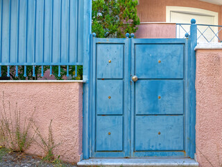 A contemporary house entrance with a blue door and bright pink fence by the sidewalk. Travel to Athens, Greece.