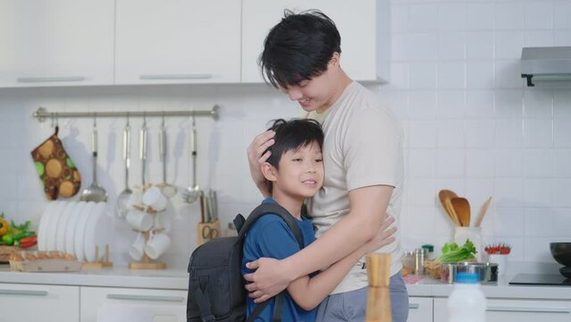 Asian cute boy back from school ran into his father was cooking dinner in the kitchen. Happy family concept
