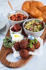 Traditional Shabbat table: challah bread, falafel, quinoa salad, hummus on a wooden board. Israeli food concept.