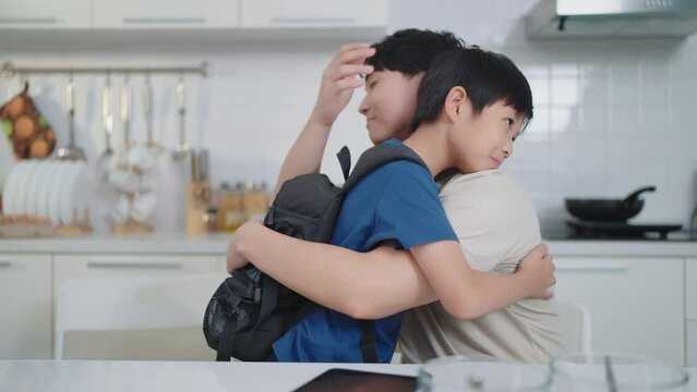 Asian cute boy back from school ran into his father sitting in the kitchen. Happy family concept