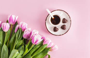 a cup of expresso coffee stands on a saucer with heart-shaped chocolates and a bouquet of lilac...