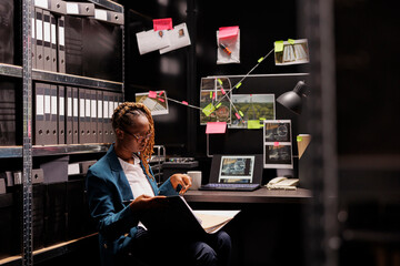 African american woman police detective studying criminal matter file while sitting at workplace...
