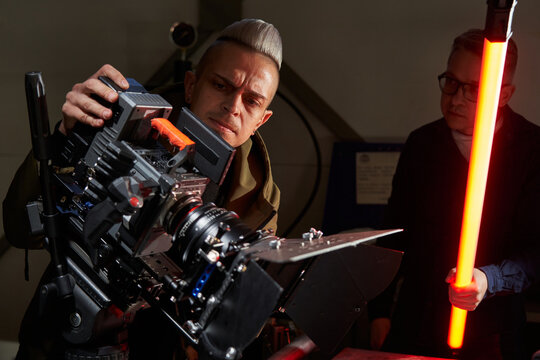 two handsome caucasian men are filming a movie on a film set with a professional movie camera with extra light astera in hand