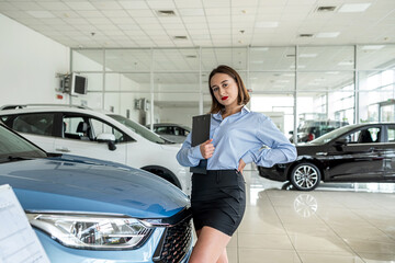 Fototapeta na wymiar female dealer near new modern car holding tablet at showroom