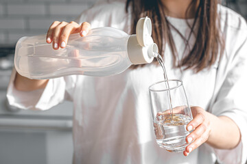 Close-up, a woman pours water into a glass.