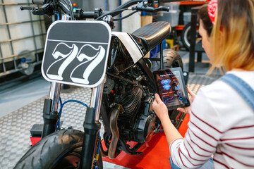 Unrecognizable mechanic woman using a diagnosis app in digital tablet to review custom motorcycle on factory
