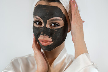 Portrait of pretty young woman wears beauty black clay mask on face isolated on white