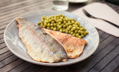 Top view of baked trout fillet served on plate with peas closeup