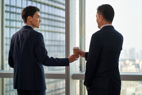 young asian businessman handing colleague a cup of coffee in modern office
