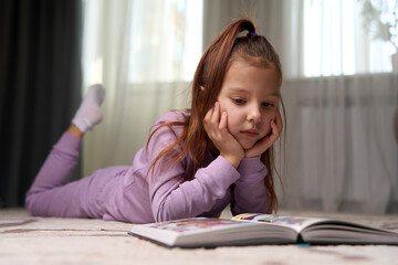 Cute girl lying on the floor and reading a book.