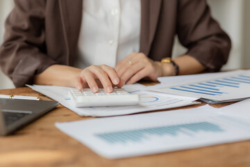Close-up shot of businesswoman using calculator and laptop to calculate company financial result On wooden table in office and business background, tax, accounting, statistics and analytical research.