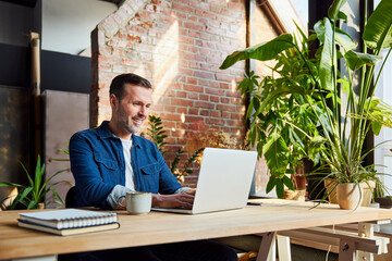 Smiling businessman working on laptop at loft office